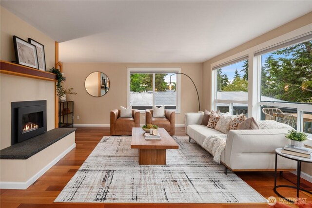 living room featuring a glass covered fireplace, baseboards, and wood finished floors