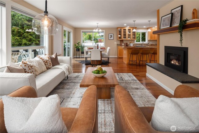 living room with baseboards, dark wood-style floors, a chandelier, a glass covered fireplace, and recessed lighting
