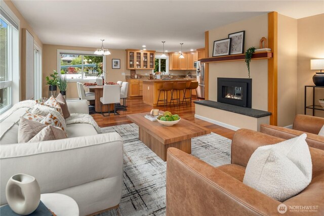 living room with light wood-style floors, an inviting chandelier, and a glass covered fireplace