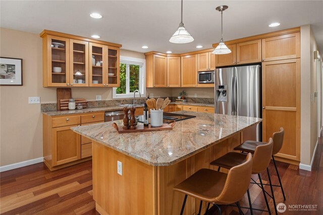 kitchen with a breakfast bar, baseboards, a sink, dark wood finished floors, and appliances with stainless steel finishes