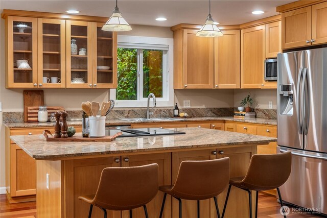 kitchen with a kitchen island, a kitchen bar, light wood-type flooring, a sink, and stainless steel appliances