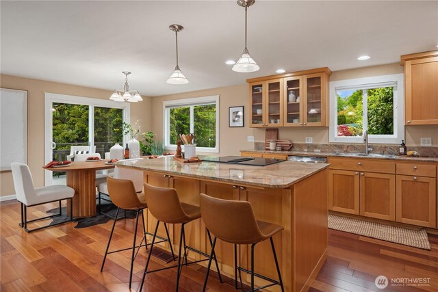 kitchen featuring light wood-style floors, a kitchen bar, a center island, black electric cooktop, and a sink