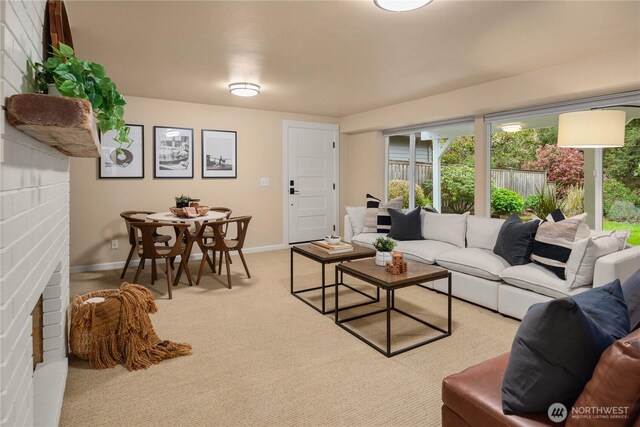 living area with a brick fireplace, baseboards, and light colored carpet