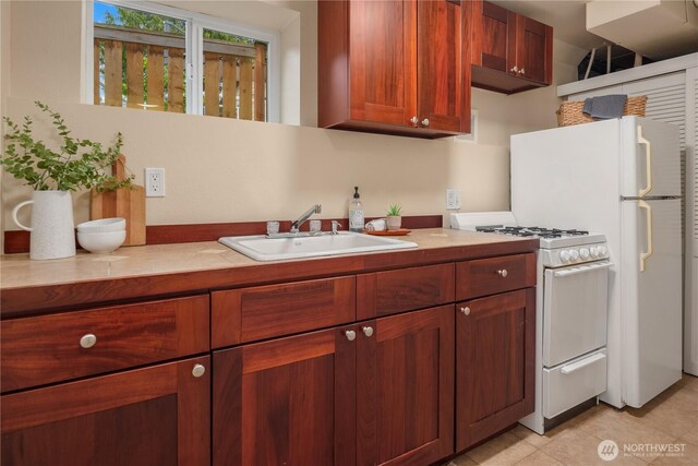 kitchen featuring light countertops, light tile patterned flooring, white gas range oven, and a sink