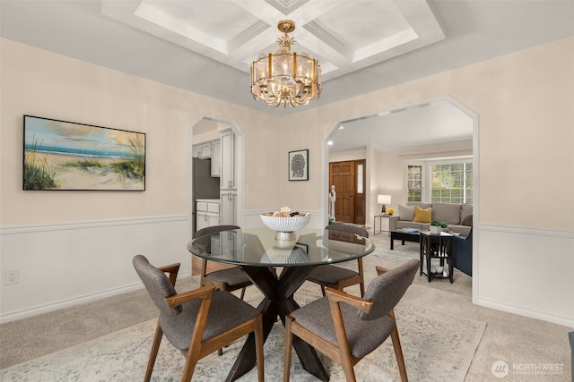dining area with light colored carpet, arched walkways, beam ceiling, a chandelier, and coffered ceiling