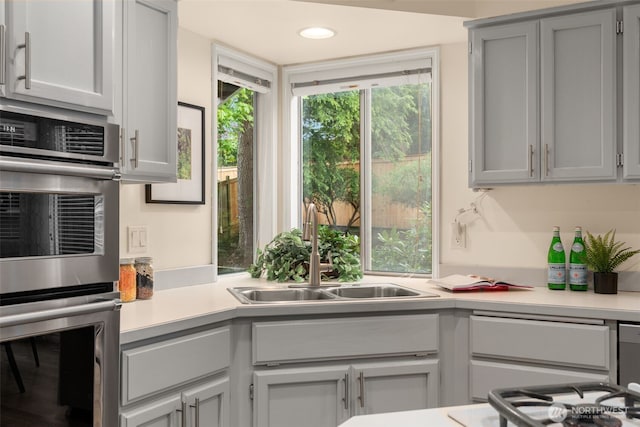 kitchen with double oven, a sink, stovetop, and light countertops