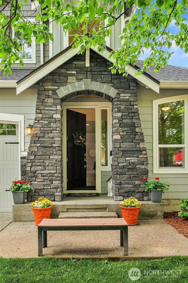 view of exterior entry with a shingled roof and stone siding