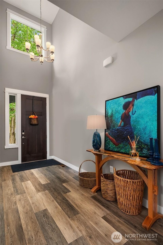 entrance foyer featuring baseboards, a high ceiling, wood finished floors, and a notable chandelier