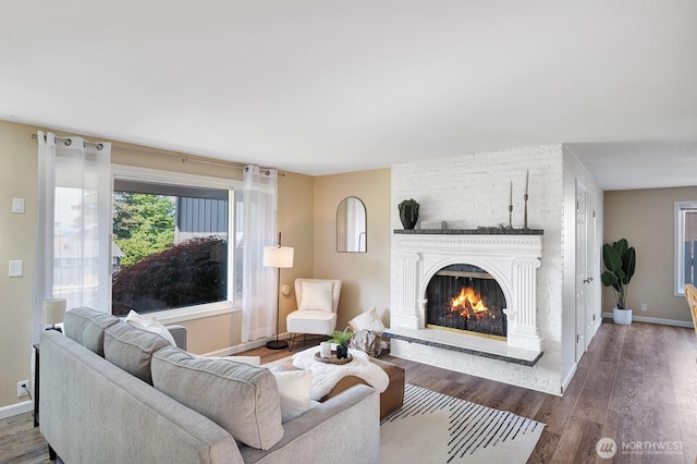 living room featuring a brick fireplace, wood finished floors, and baseboards