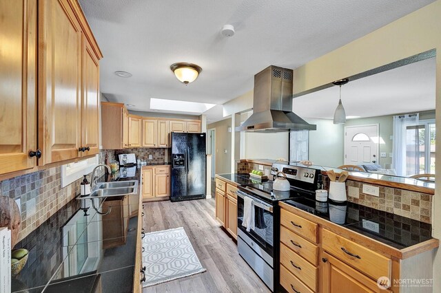 kitchen with black fridge, stainless steel electric stove, island range hood, a sink, and backsplash