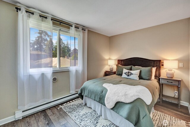 bedroom with a baseboard radiator, wood finished floors, and baseboards