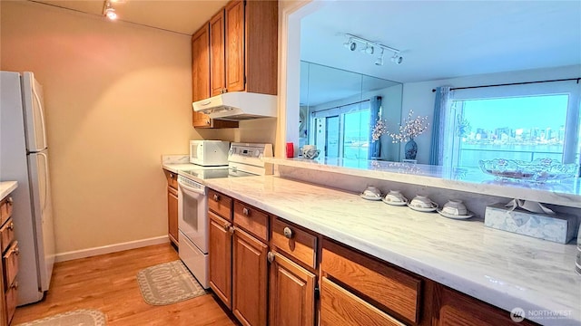 kitchen with white appliances, brown cabinetry, under cabinet range hood, and track lighting