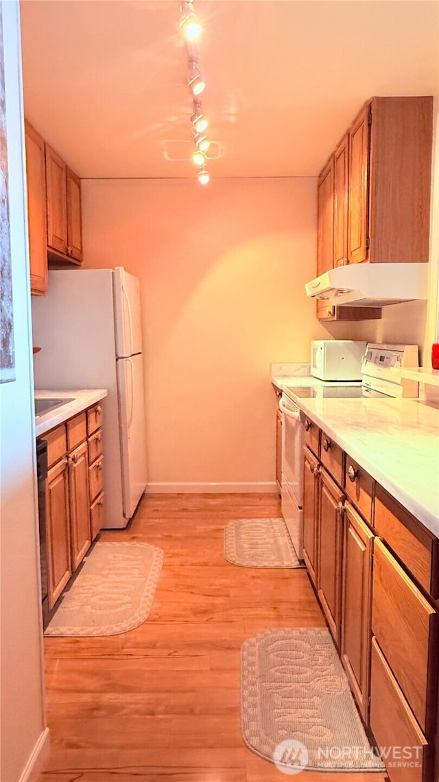 kitchen with baseboards, light wood-type flooring, under cabinet range hood, and white appliances