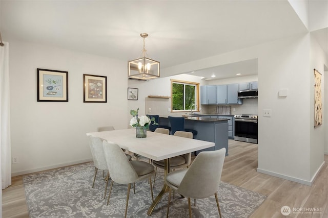 dining space with light wood-type flooring, recessed lighting, baseboards, and a notable chandelier