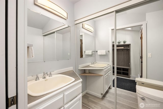bathroom featuring a sink, baseboards, wood finished floors, and two vanities