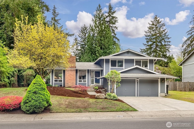 tri-level home with a garage, fence, a front yard, a chimney, and concrete driveway