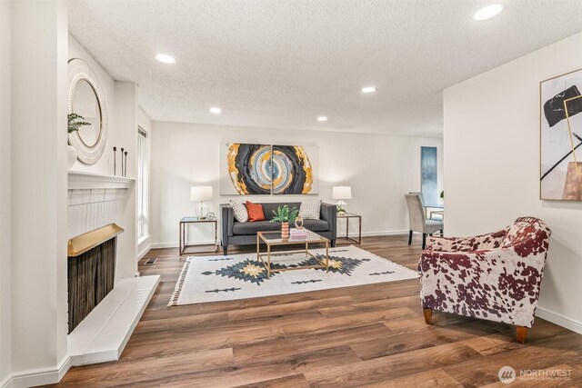 living area with a textured ceiling, wood finished floors, baseboards, a fireplace with raised hearth, and recessed lighting