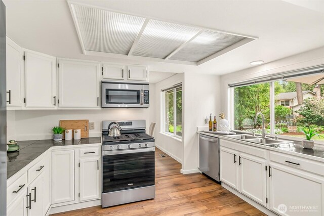 kitchen with light wood-style floors, baseboards, white cabinetry, a sink, and appliances with stainless steel finishes