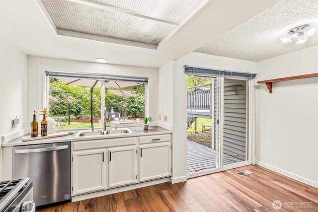 kitchen with appliances with stainless steel finishes, wood finished floors, a sink, light countertops, and white cabinetry