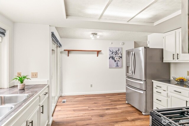 kitchen featuring white cabinets, stainless steel fridge, a sink, light wood-style flooring, and baseboards