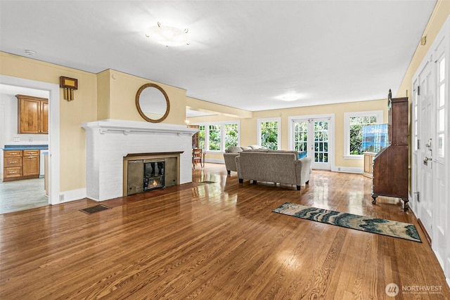 living room featuring a fireplace, french doors, baseboards, wood finished floors, and visible vents