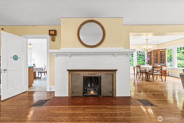 living room featuring visible vents, a brick fireplace, wood finished floors, and a notable chandelier