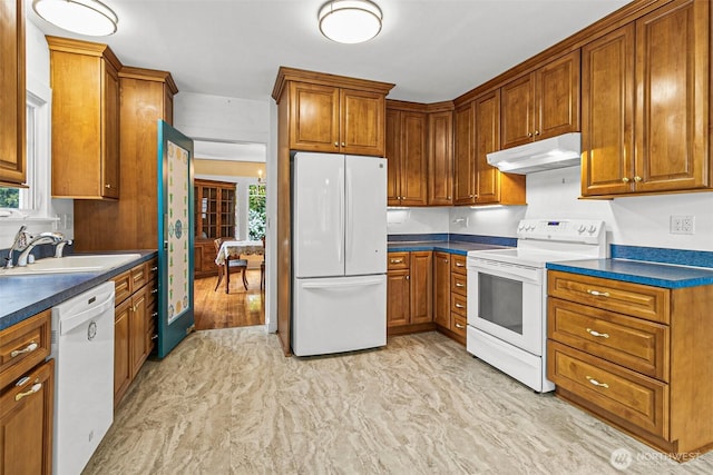 kitchen featuring brown cabinetry, under cabinet range hood, and white appliances