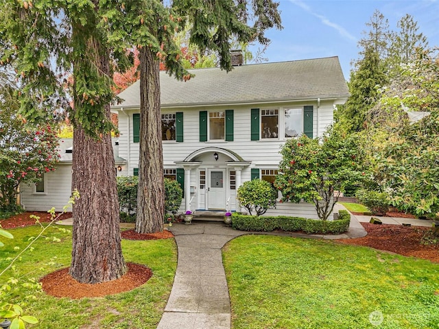 colonial inspired home with a chimney, a shingled roof, central AC, and a front yard