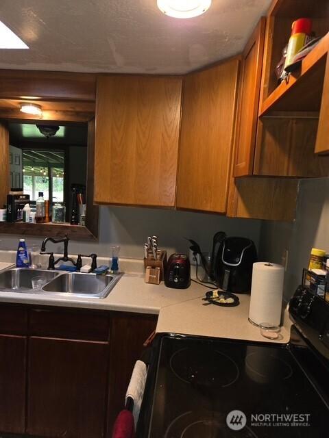 kitchen with a sink, brown cabinets, black electric range, and light countertops