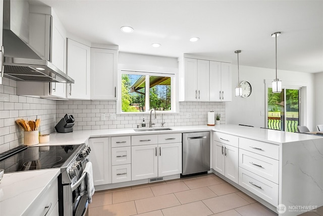 kitchen with wall chimney range hood, appliances with stainless steel finishes, a sink, a peninsula, and visible vents