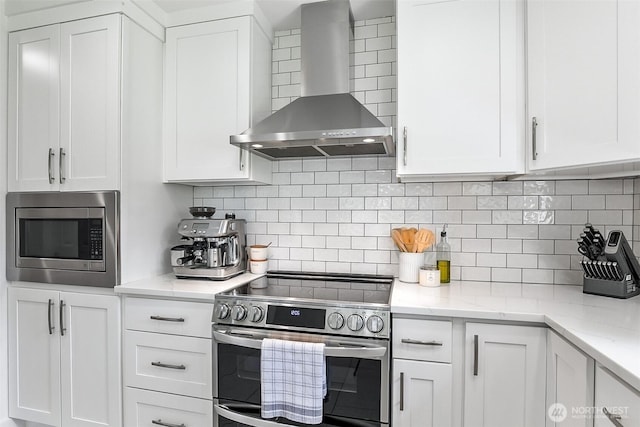 kitchen featuring light stone countertops, wall chimney range hood, white cabinets, tasteful backsplash, and stainless steel appliances