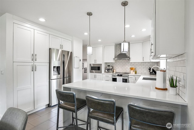 kitchen featuring wall chimney range hood, appliances with stainless steel finishes, a sink, a peninsula, and tasteful backsplash