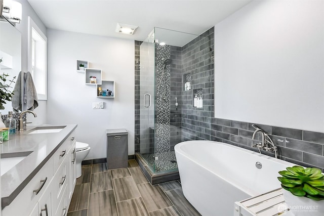bathroom featuring double vanity, a shower stall, a sink, toilet, and a soaking tub