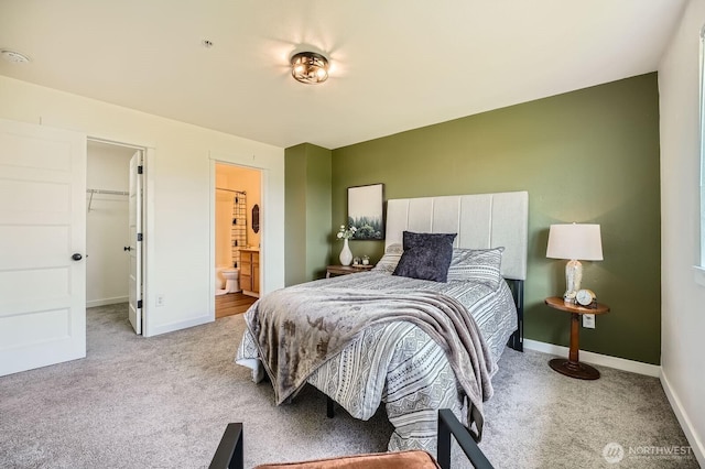 carpeted bedroom with baseboards, ensuite bathroom, and a walk in closet