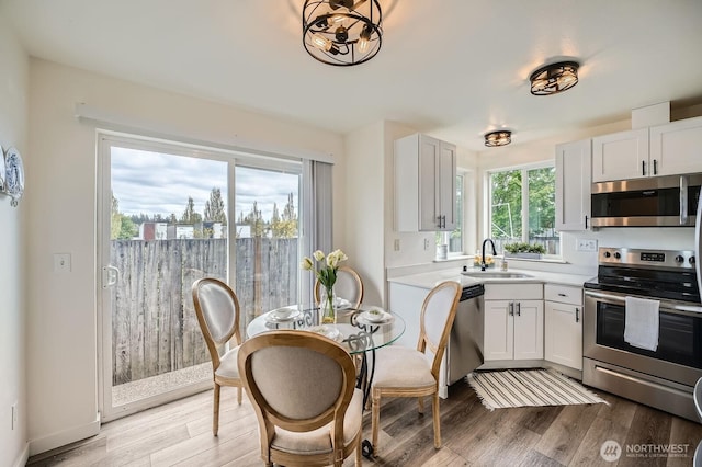 kitchen featuring light countertops, white cabinets, a sink, light wood finished floors, and appliances with stainless steel finishes