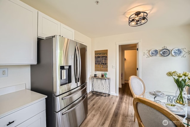 kitchen featuring light countertops, light wood-type flooring, stainless steel refrigerator with ice dispenser, and white cabinetry