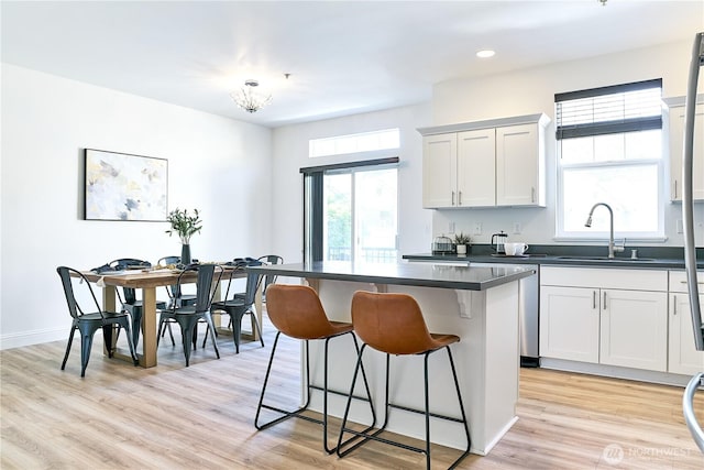 kitchen featuring dark countertops, a breakfast bar, a sink, light wood-style flooring, and a kitchen island