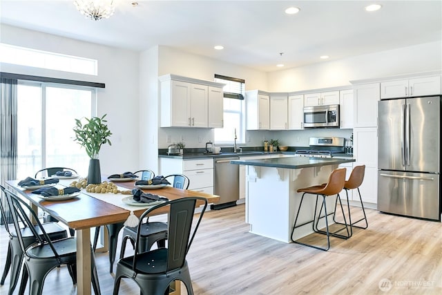 kitchen featuring dark countertops, appliances with stainless steel finishes, a sink, a center island, and a kitchen bar