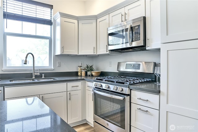 kitchen featuring a sink, appliances with stainless steel finishes, white cabinets, and dark countertops