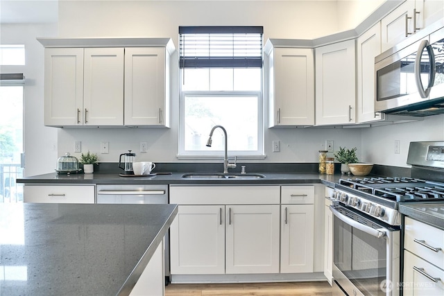 kitchen featuring a sink, dark stone countertops, appliances with stainless steel finishes, and light wood finished floors