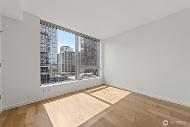 spare room featuring wood finished floors, a city view, and baseboards