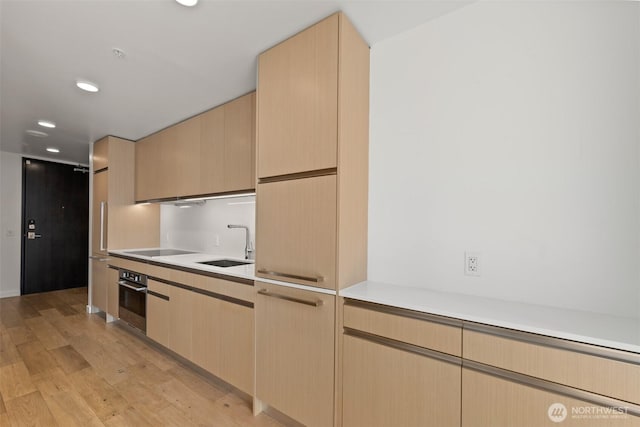 kitchen with oven, a sink, light countertops, light wood-style flooring, and light brown cabinets