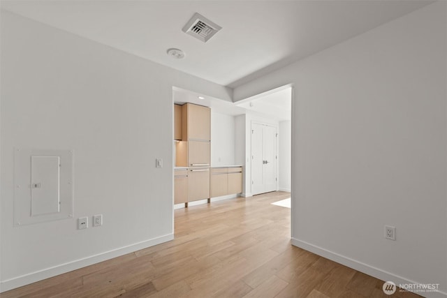 unfurnished room featuring baseboards, light wood finished floors, and electric panel