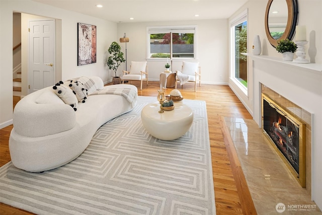 living area featuring light wood-style flooring, stairs, recessed lighting, baseboards, and a high end fireplace