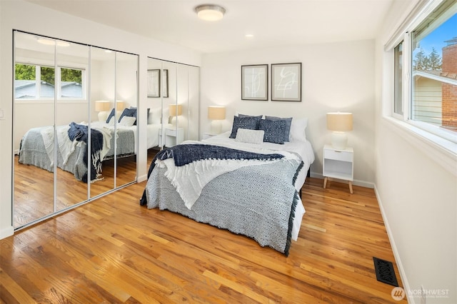 bedroom featuring two closets, baseboards, visible vents, and wood finished floors