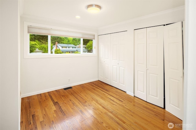 unfurnished bedroom featuring light wood finished floors, two closets, baseboards, visible vents, and ornamental molding