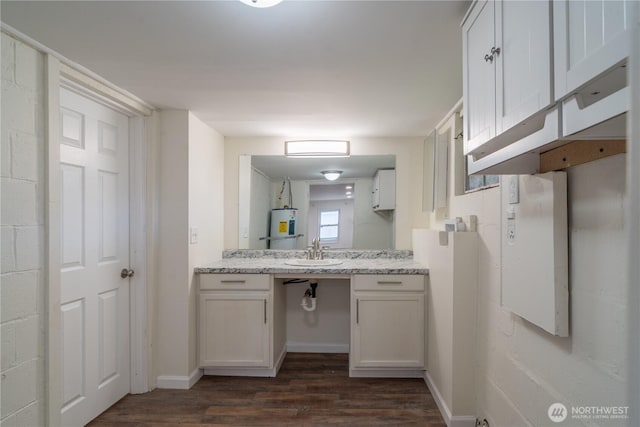 kitchen featuring dark wood-style flooring, light stone countertops, a sink, baseboards, and water heater