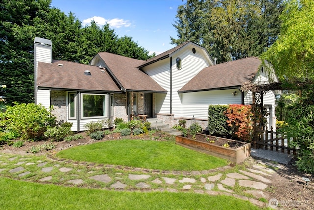 view of front of property with a chimney, a front yard, brick siding, fence, and a shingled roof