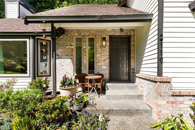 entrance to property with a shingled roof, a porch, and brick siding
