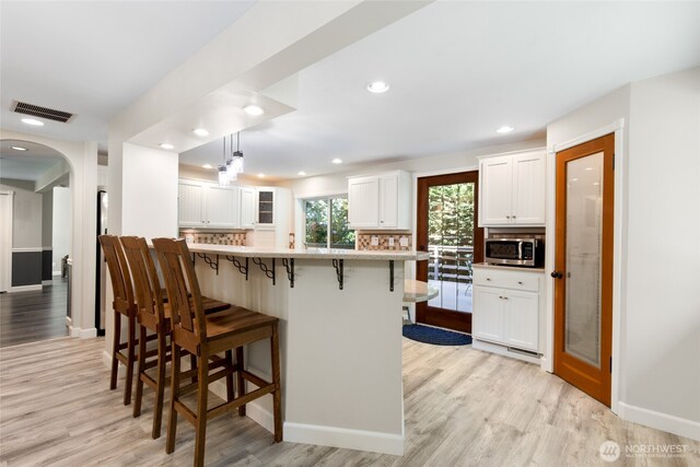 kitchen featuring a breakfast bar area, light wood-style flooring, white cabinetry, stainless steel microwave, and tasteful backsplash